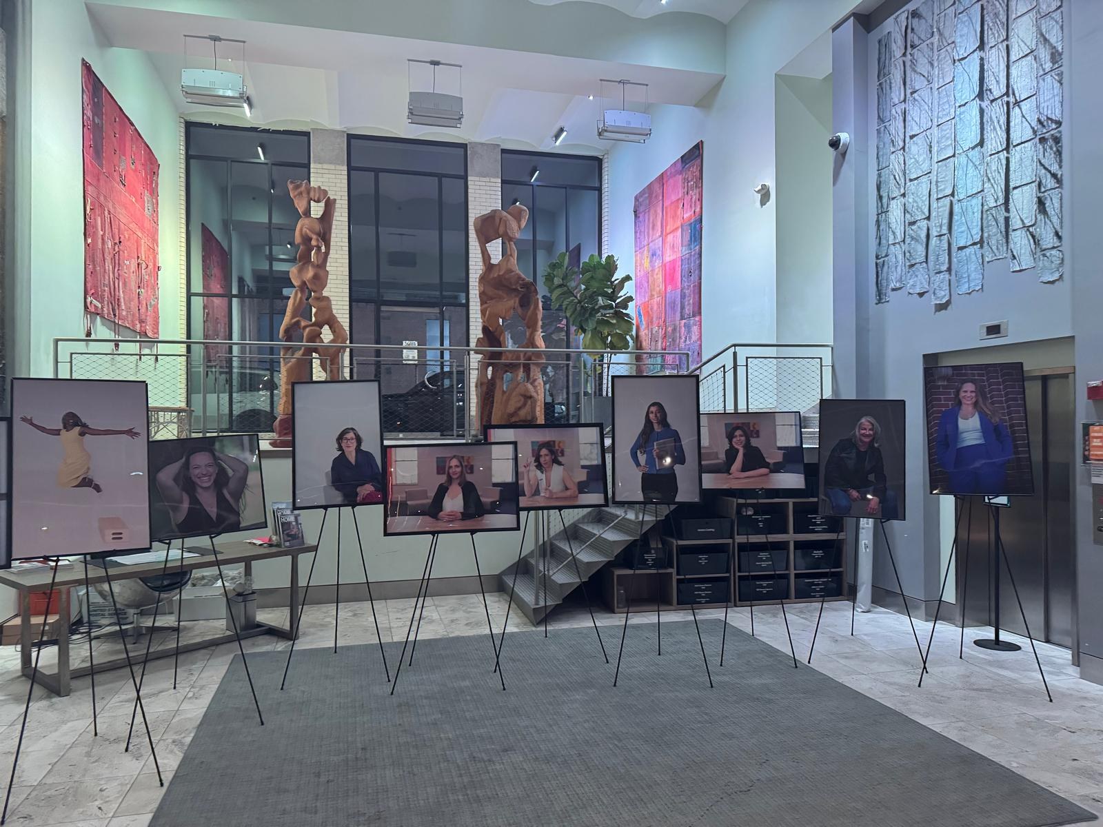 Large framed portraits of women founders displayed on easels in a building lobby, part of an #AtTheTable exhibit
